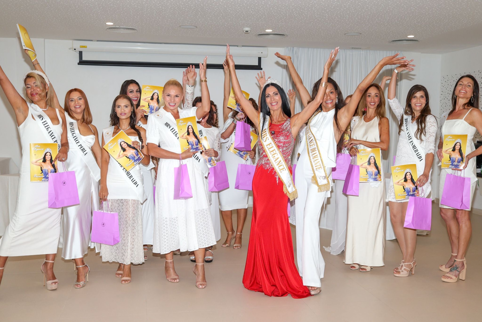 Grupo de mujeres celebrando en un escenario con ejemplares de Mrs Elegance y bolsas de regalo